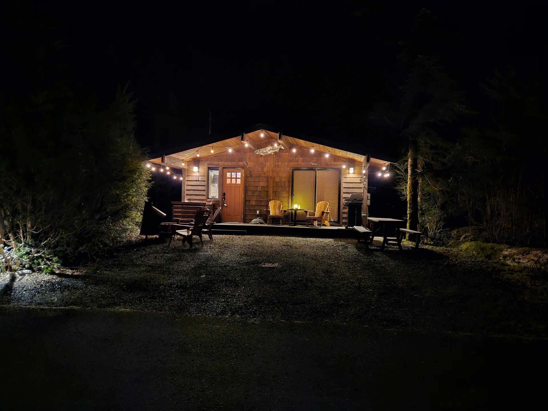 Wide view of Rachael's Retreat cabin lit up at night with Adirondack chairs