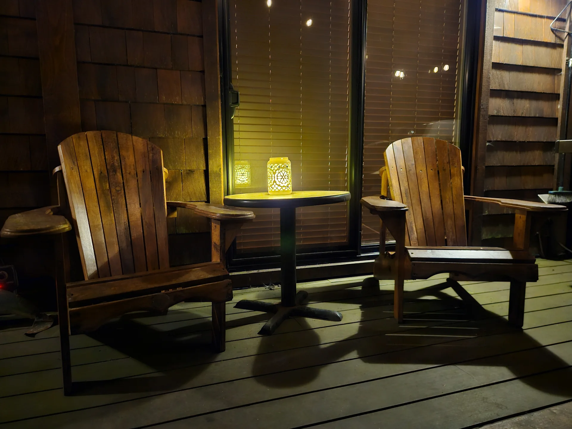 Covered porch with two Adirondack chairs and lantern at night